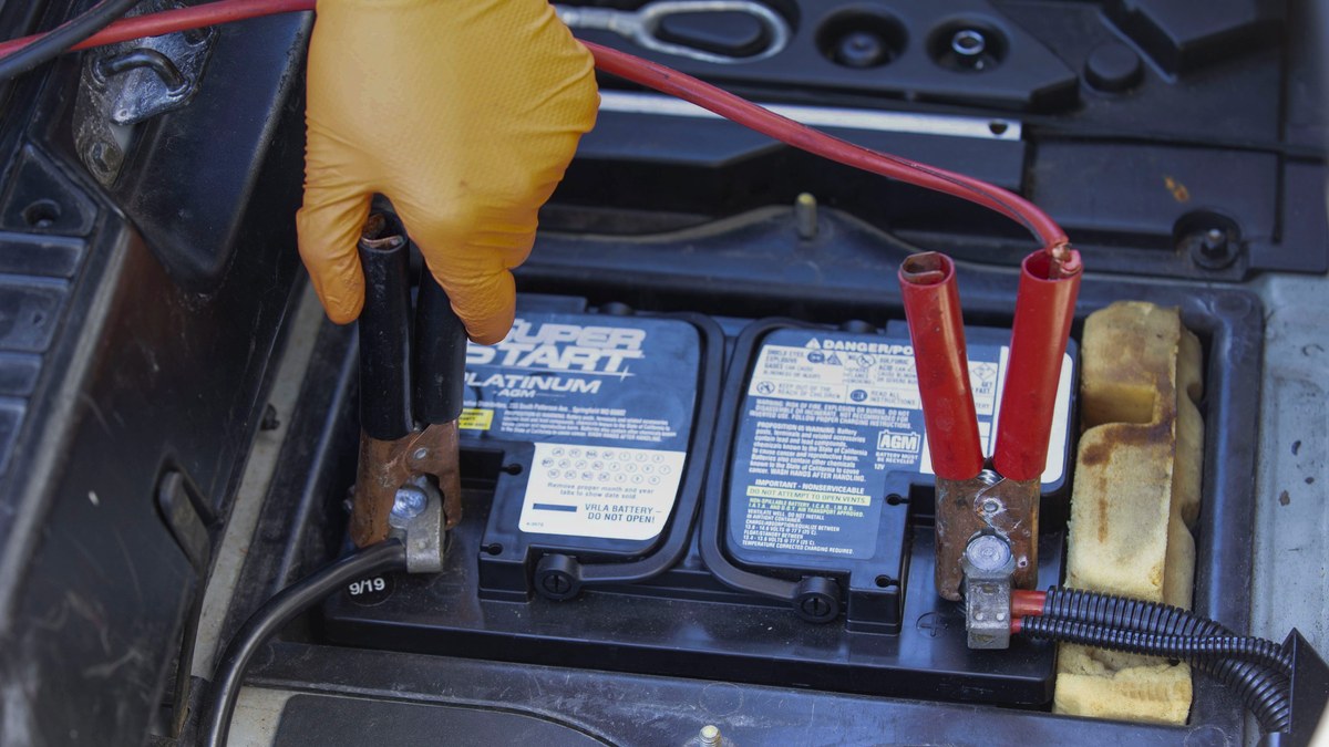 Close-up of hands inspecting corroded jump starter clamps for damage before repair