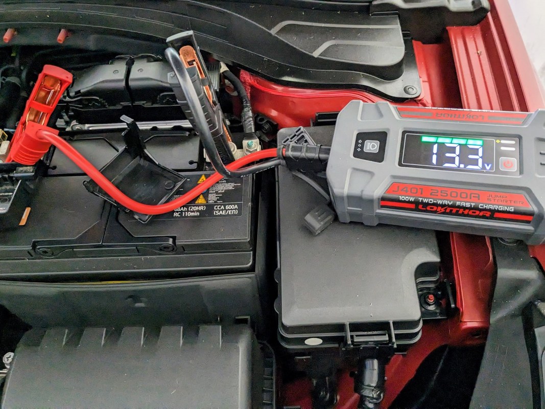 Close-up of hands comparing voltage specifications on a jump starter and car battery label.