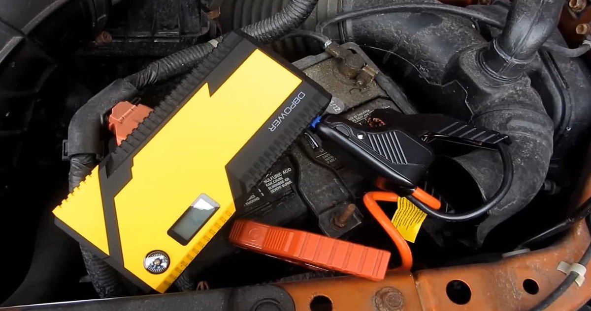 A portable jump starter with jumper cables clamped to a car battery, device screen displaying an error indicator.